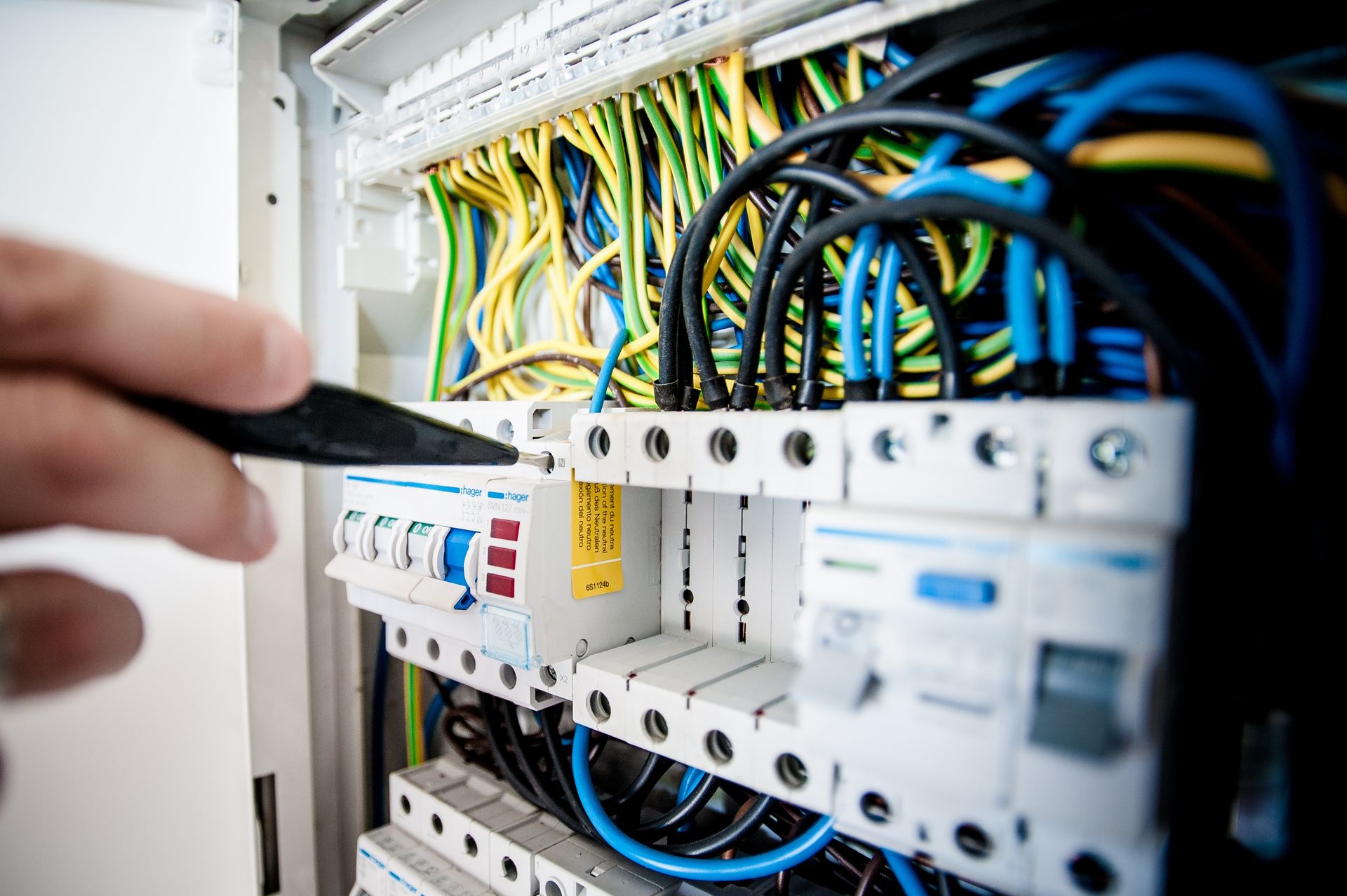 Close-up of an electrician's hands fitting a circuit breaker into a consumer unit, surrounded by coloured wiring