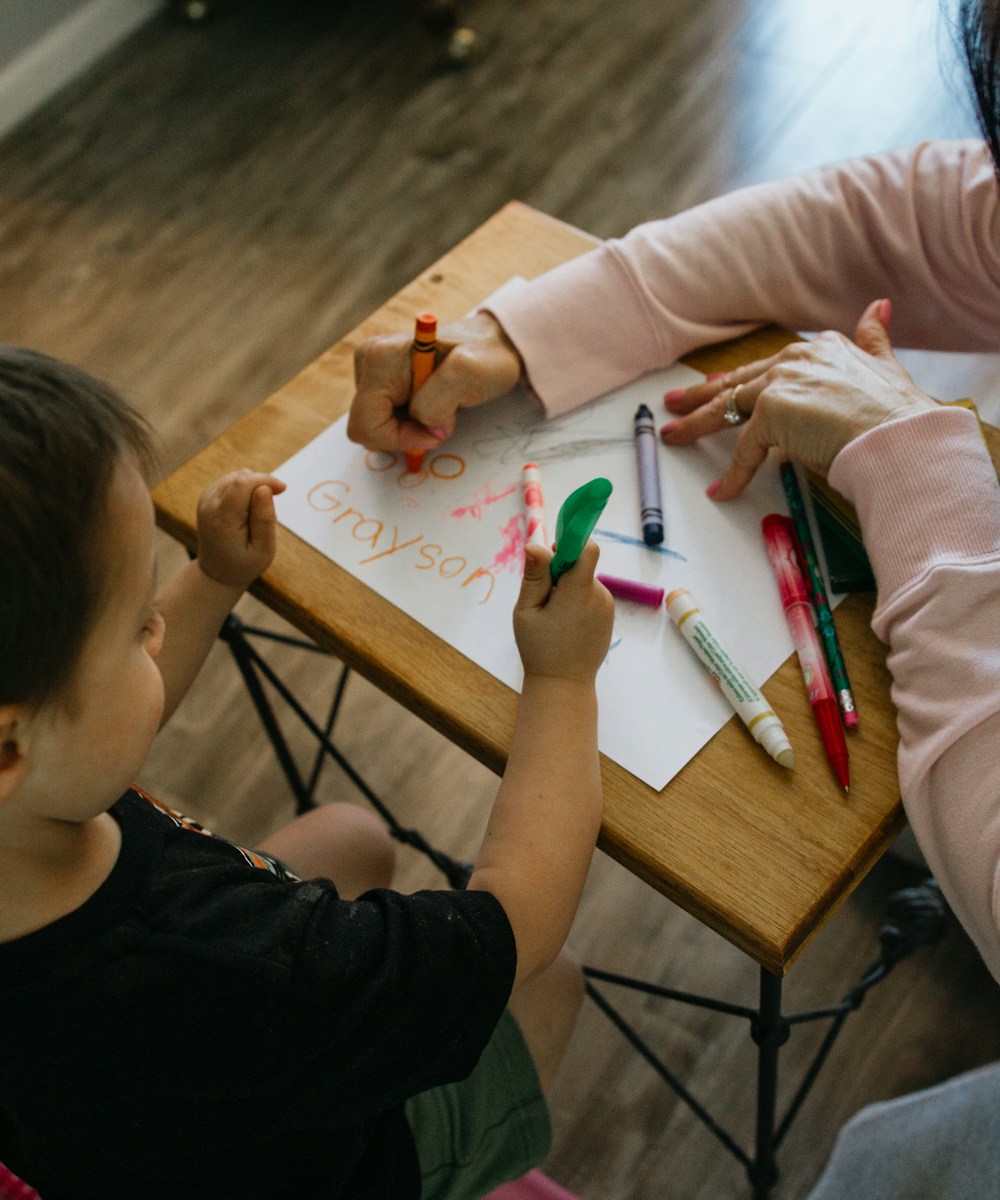 A carer helping a young child with drawing and colouring at Nellie's Daycare