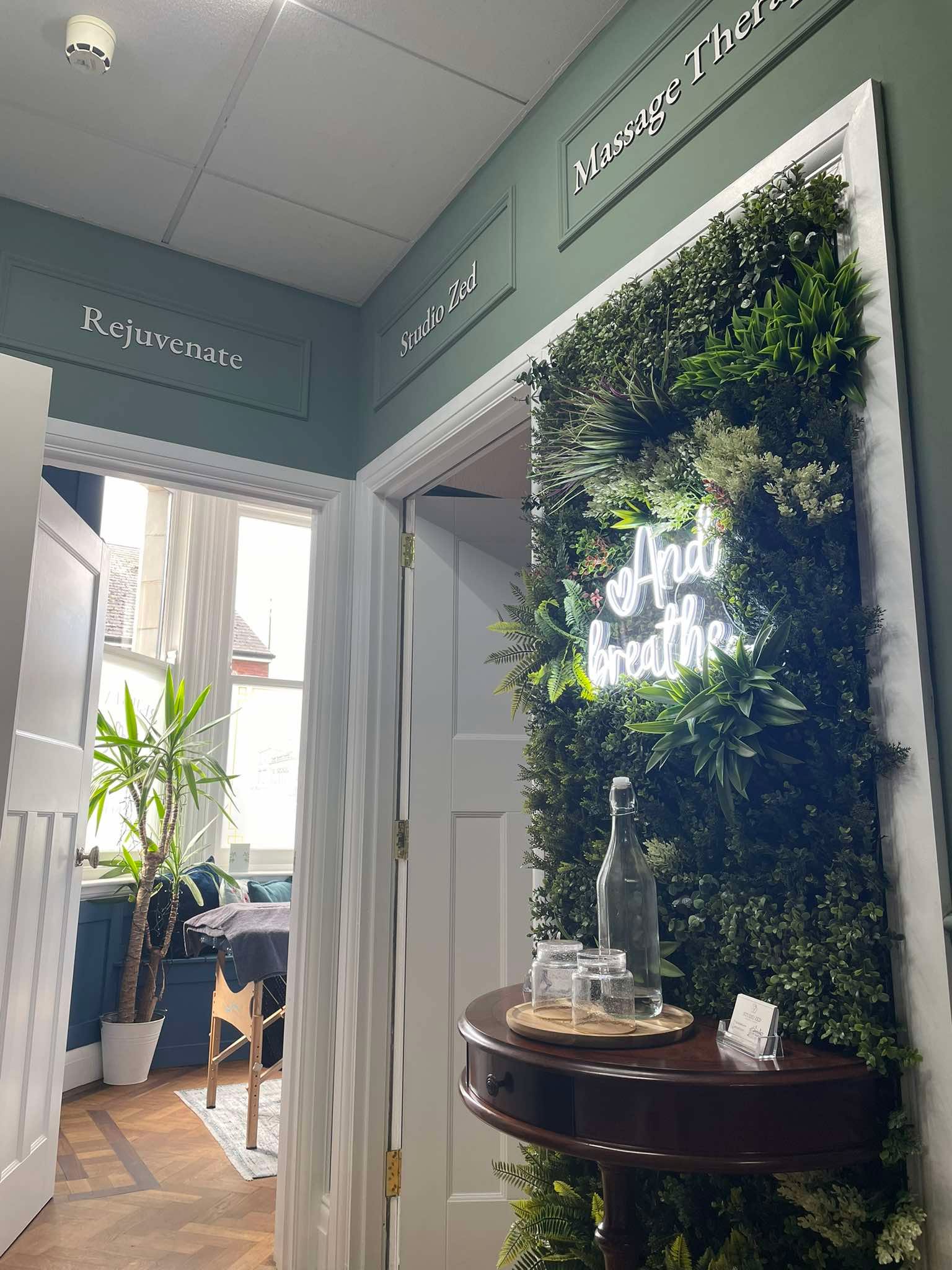 Entrance to Rejuvenate Massage Therapy with living plant wall and neon "And breathe" sign